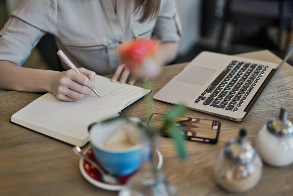 A person focused on their work, making notes in a planner with a laptop nearby.